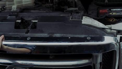 woman in early 20s checking under the hood of a truck and going under the truck to find and fix mechanical problem