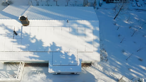 high angle drone shot in front of snowy pv panels, sunny winter day at a rural house