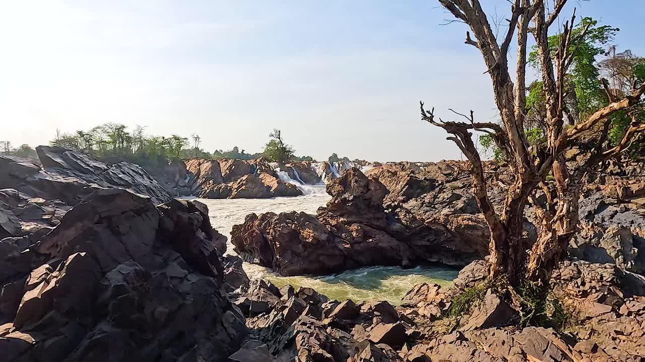 A serene landscape of Khone Phapheng Falls with rocky terrain and flowing water under bright daylight in Champasak, Laos