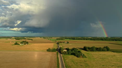 aerial view of cloudburst in countryside of latvia, agricultural meadow covered in sunshine