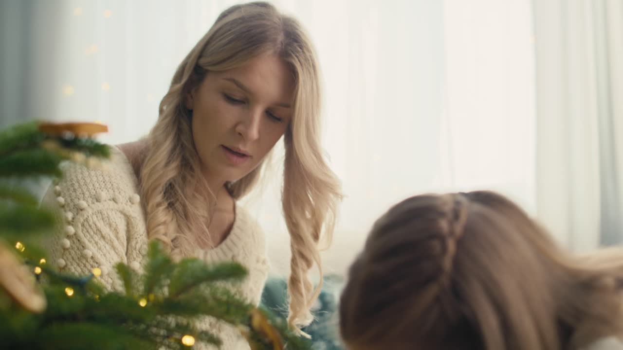 백인 어린 소녀와 어머니가 크리스마스 트리를 장식하고 있습니다.