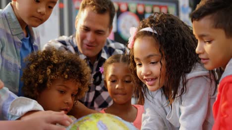 vista frontal del maestro caucásico enseñando a los niños sobre el globo en el aula 4k