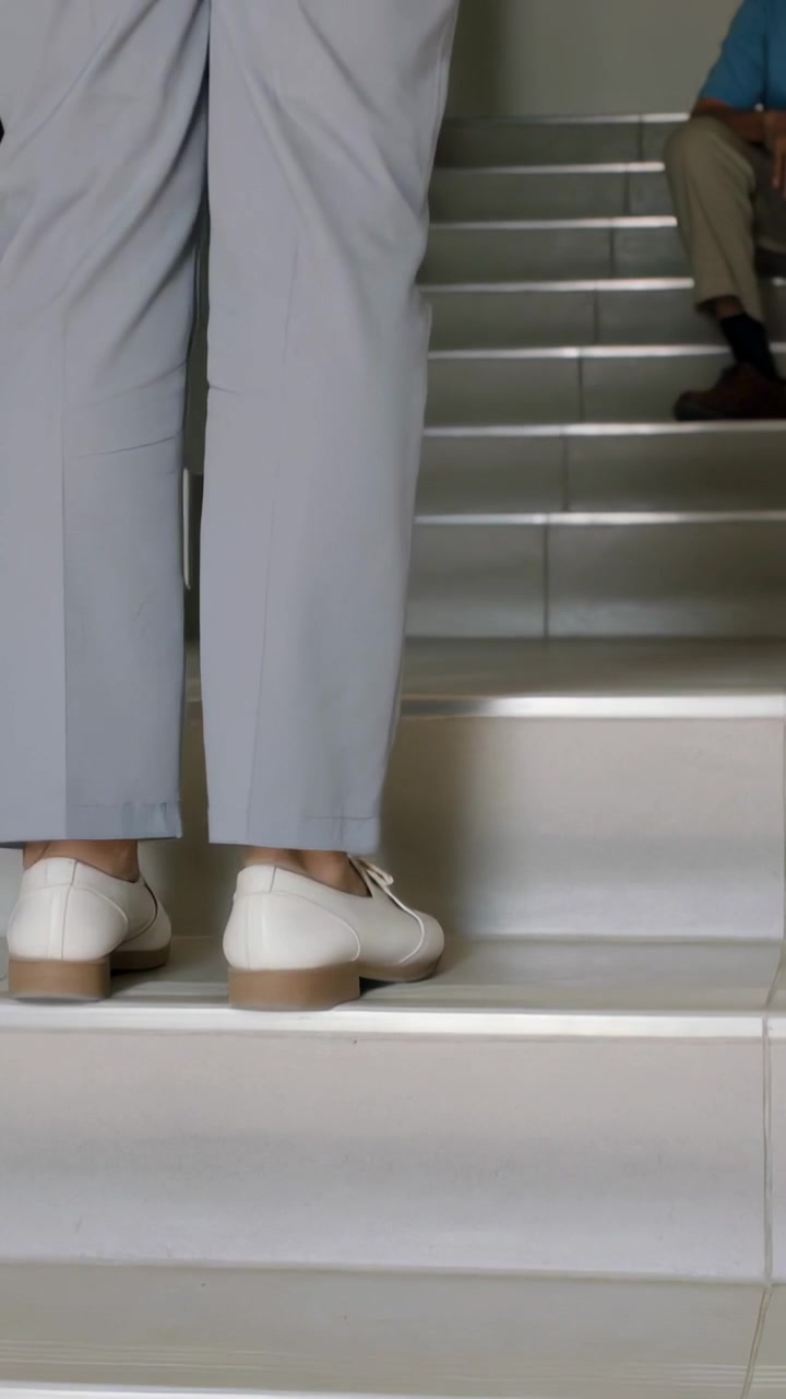 Vertical video: Lifting right foot, man climbing stairwell toward landing in shoes and gray pants