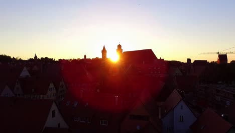 aerial flies over the old city against the sunset and the sun showing between the church and the tower