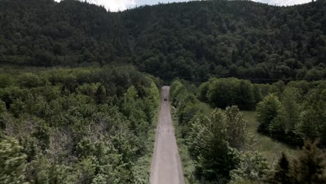 Viaje-Por-Carretera-En-Coche-Infiniti-A-Través-Del-Exuberante-Sendero-Verde-Que-Se-Dirige-Hacia-La-Pintoresca-Montaña-En-Un-Día-Soleado---Toma-De-Drones