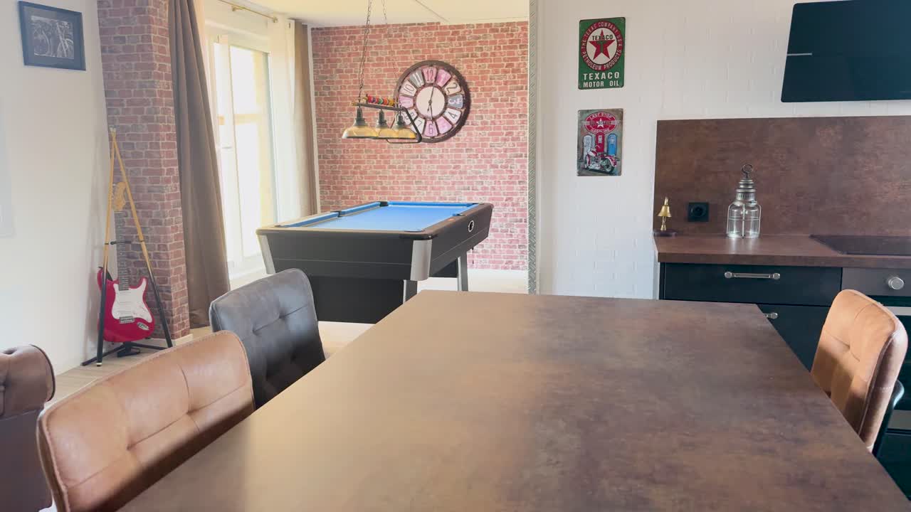 Camera slowly pans across a retro-inspired apartment kitchen and lounge, revealing a billiard table, vintage decor, and warm natural lighting
