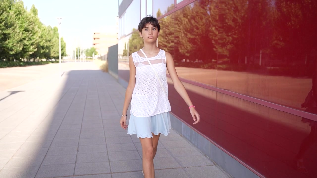Una giovane ragazza cammina felicemente e con aria sognante e allegra accanto a una splendida architettura moderna.