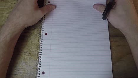 person looking down at a paper note book with a pen in hand not knowing what to write