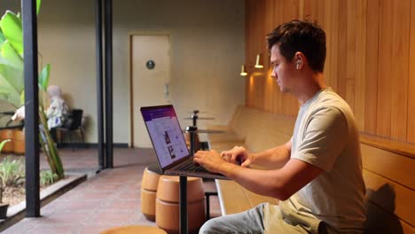 nómada digital trabajando en una computadora portátil moderna dentro de una cafetería - vista de perfil