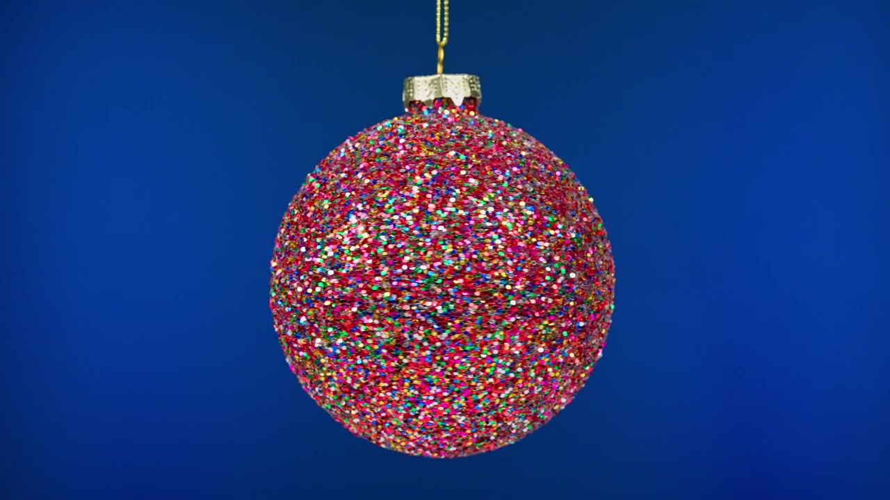 Glitzernde rote Weihnachtsbaumkugel vor blauem Hintergrund hängend