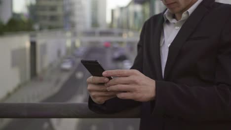 Side-view-of-male-hands-leaning-on-banister,-texting-on-tablet