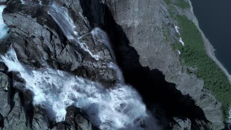 aerial top down shot of massive water flowing down waterfall trolltunga in norway - forest woodland in the valley