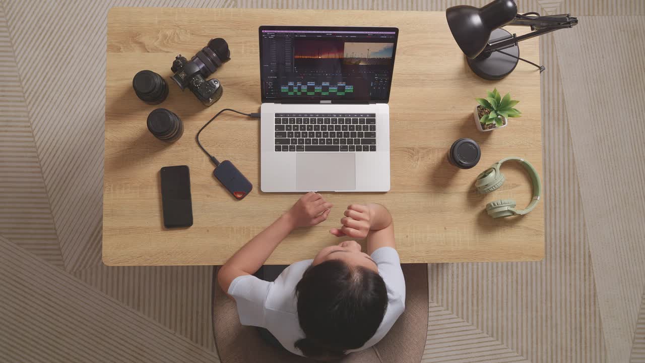 Top View Of Asian Woman Editor Yawning And Sleeping While Sitting In The Workspace Using A Laptop Next To The Camera Editing The Video At Home