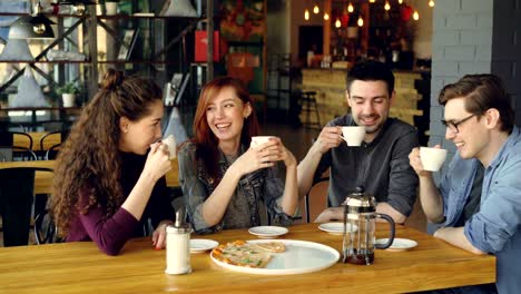 los amigos están celebrando la reunión en el café con bebidas y pizza, tazas sonando, bebiendo y compartiendo noticias. amistad, estilo de vida moderno, comunicación y concepto de celebración.