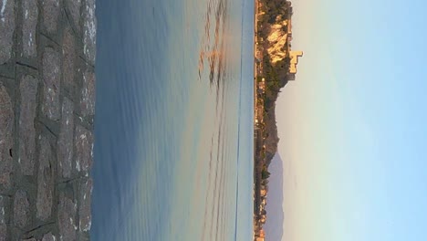 Back-view-of-woman-sitting-on-jetty-facing-lake-and-castle