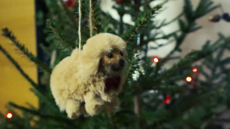 funny little and fluffy dog christmas decoration hanging on a christmas tree with red led lights lighting the pine needles in the background. camera slowly pans around the decoration in close up.