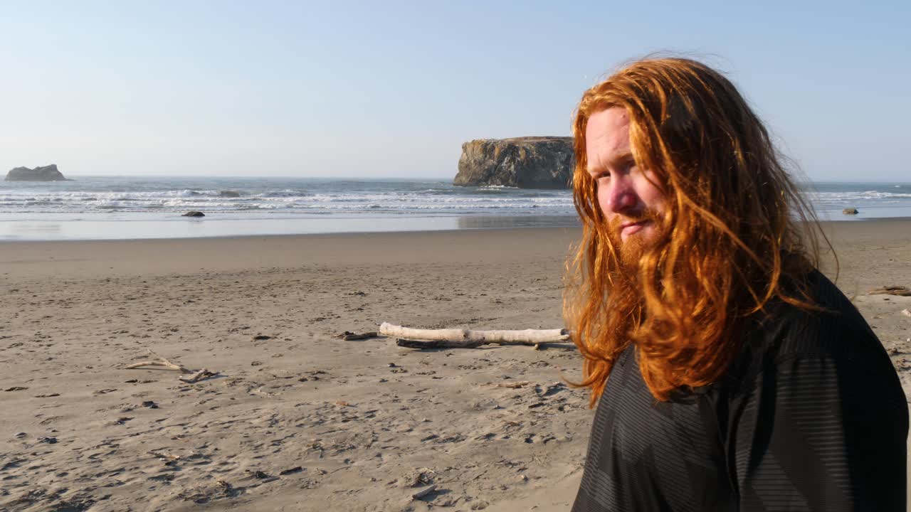 긴 붉은 머리를 가진 남자가 오레곤의 해변을 조용히 바라보고 있다