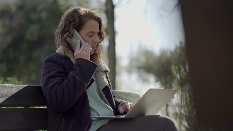 mujer de mediana edad reflexiva hablando en un teléfono inteligente al aire libre