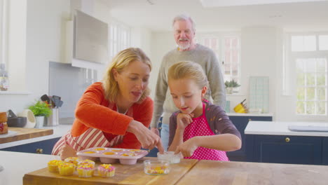 Abuelos-Con-Nieta-Divirtiéndose-Decorando-Pasteles-Caseros-En-La-Cocina