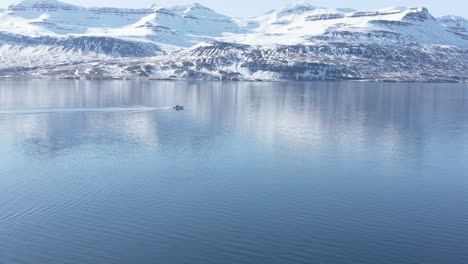 el barco viaja a través del fiordo en islandia, montañas cubiertas de nieve en segundo plano.