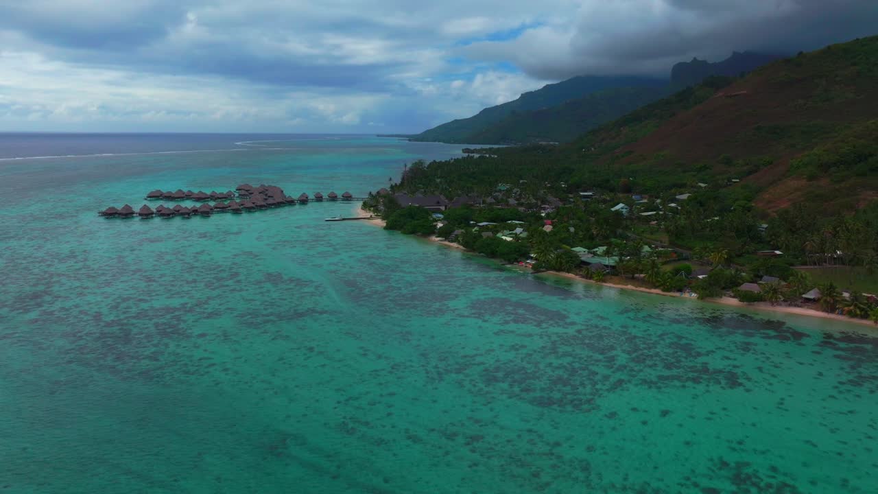 Luftfoto fra drone af bungalows over vandet på Moorea, Fransk Polynesien, med roligt turkist lagunevand, der strækker sig langs Opunohu-bugten ved siden af en fredelig tropisk kystlinje, med baglæns bevægelse.