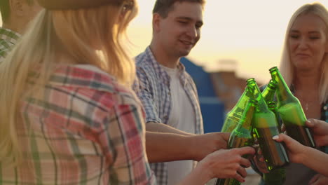 American-people-clinks-glasses-and-drinks-beer-from-green-bottels-on-the-party-with-friends-on-the-roof.-Women-is-drinking-cold-beer-after.