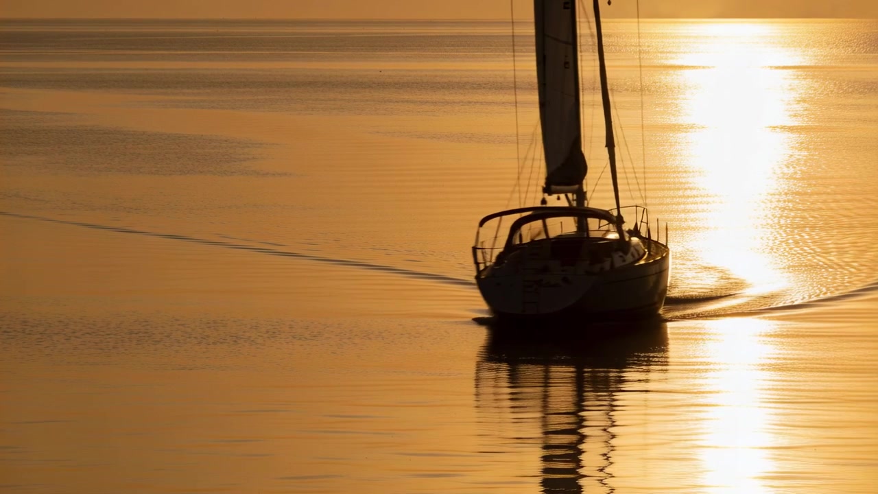 Barca a vela che scivola con una leggera brezza che spinge verso la telecamera sull'acqua al tramonto, con il riflesso del sole.