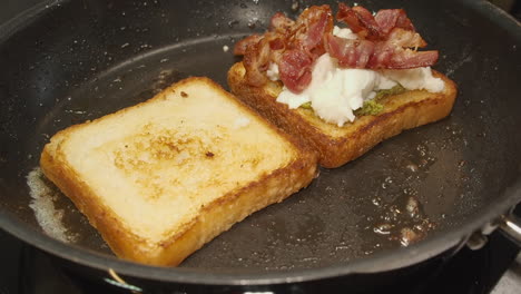 Crispy-bacon-added-to-cheese-and-pesto-on-fried-sandwich-bread-in-pan