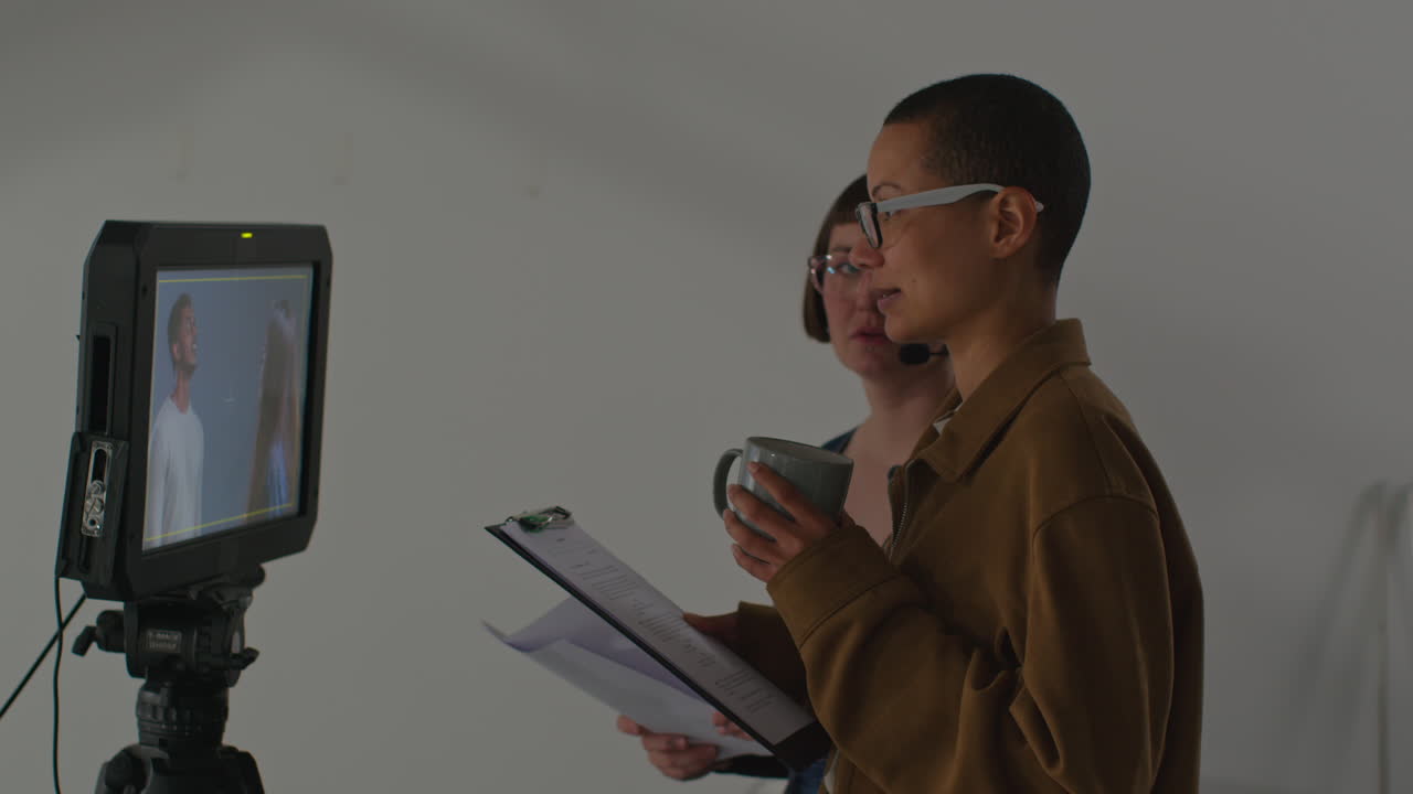 una directora en un set de cine, mirando un monitor y sosteniendo un guión