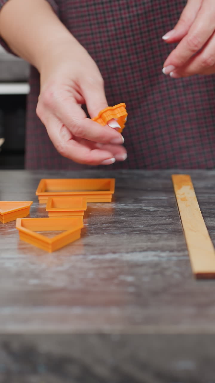 primer plano de un panadero colocando formas de horneado de naranja en la encimera con papel marrón al lado, preparándose para la creación de pasteles en un entorno de cocina moderno