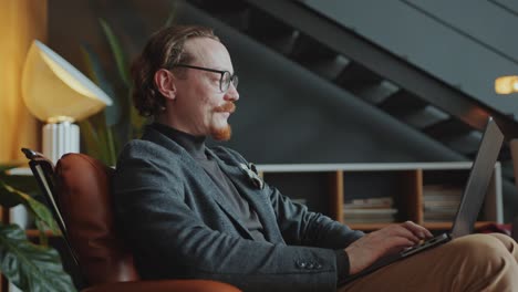 businessman sitting in armchair and typing on laptop during workday in office