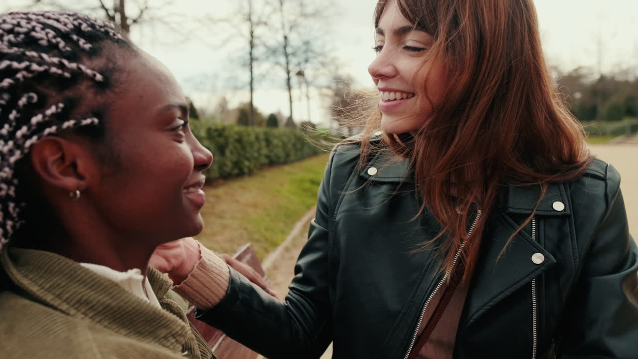 Two Happy Diverse Women Smiling and Talking on a Park Bench