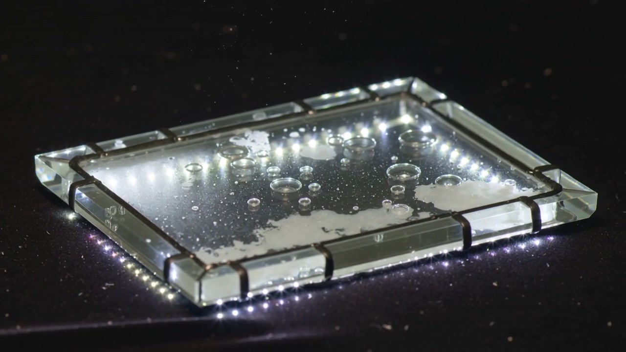 Telecamera che si sposta ruotando in senso orario su un tavolo nero, mostrando un piatto trasparente con bolle e un bordo LED.