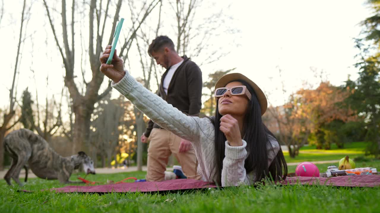 Frau macht ein Selfie, während sie mit Partner und Hund im Park entspannt