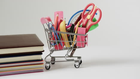 cerrar el carrito de compras con artículos escolares y pila de libros en fondo gris
