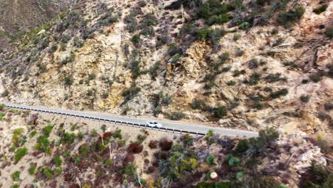 un auto blanco en un viaje de placer a lo largo de un pintoresco camino montañoso sinuoso - seguimiento aéreo