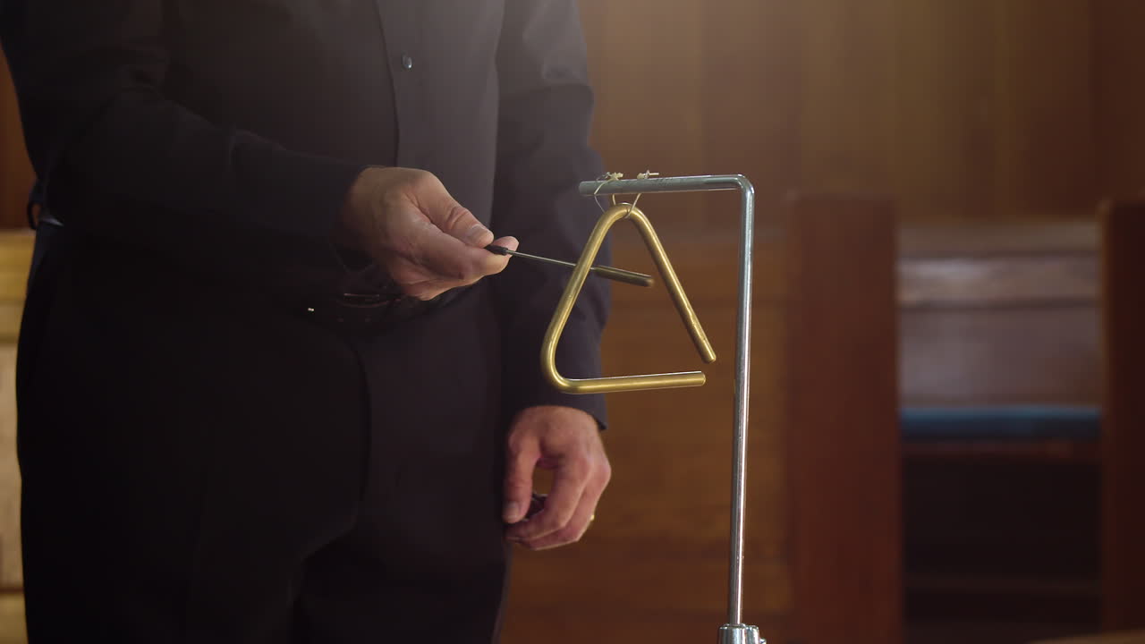 공식적인 검은 양복을 입고 삼각형 악기를 연주하는 타악기 연주자