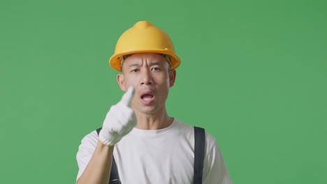 close up of asian man painter wearing safety helmet shouting to camera while standing in the green screen background studio