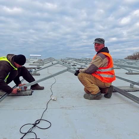 construction of solar farm on flat roof under the sky. men installers build metal base for future innovative electricity power plant. alternative energy.