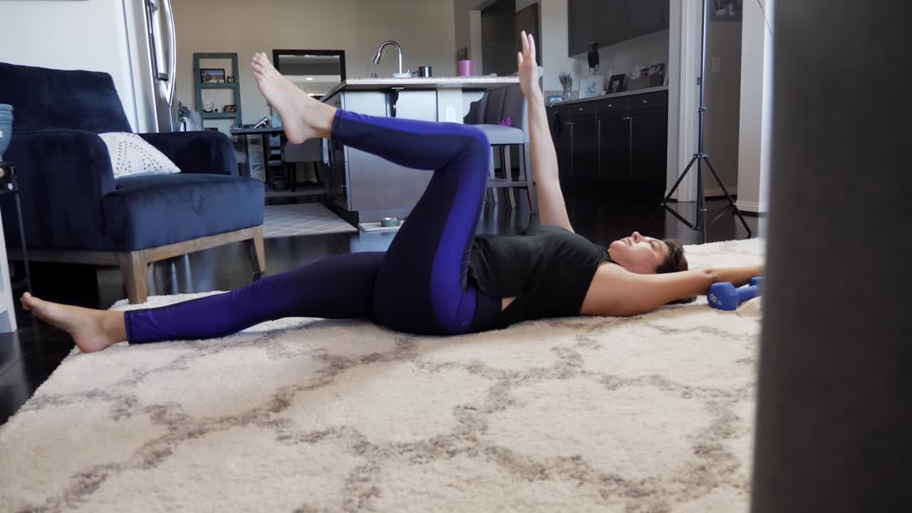 Young female working out in living room on white rug, near kitchen, sliding reveal view