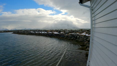 Tiro-Pov-Caminando-Por-El-Edificio-Del-Puerto-Con-Vistas-Al-Rompeolas-Y-Revelando-El-Mar,-Las-Nubes-Y-Las-Montañas-Cubiertas-De-Nieve,-Puerto-De-Åse,-Andoya,-Noruega