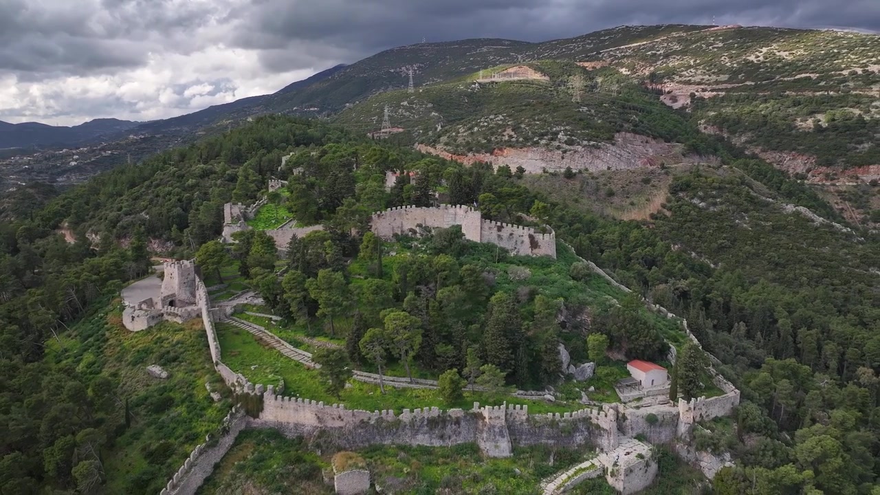 Ripresa aerea con drone ad alta quota che si allontana per rivelare le imponenti mura del castello veneziano di Nafpaktos, costruito su una collina ricoperta di pini sotto un cielo nuvoloso a Lepanto, Etolia-Acarnania, Grecia.