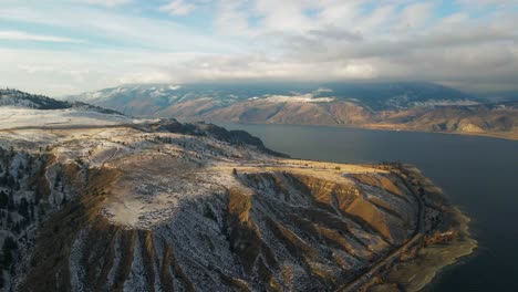 A-Medida-Que-El-Sol-Comienza-A-Ponerse-Sobre-El-Lago-Kamloops-En-Invierno,-La-Luz-De-La-Hora-Dorada-Ilumina-El-Terreno-Desértico-Montañoso-Parcialmente-Cubierto-De-Nieve-Alrededor-Del-Lago