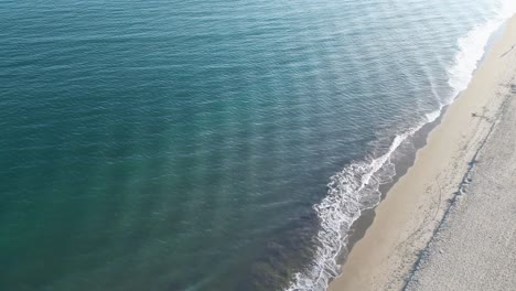 Drone-footage-of-ocean-waves-crashing-gently-against-the-beach-at-sunset-with-people-walking-on-the-shoreline