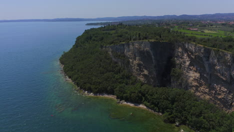 Toma-Aérea-Alejándose-De-Los-Acantilados-De-Manerba-En-El-Lago-Di-Garda-En-Un-Día-Soleado