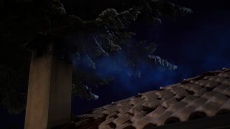 humo de chimenea sobre la casa del techo y el abeto cubierto de nieve en una fría noche de invierno