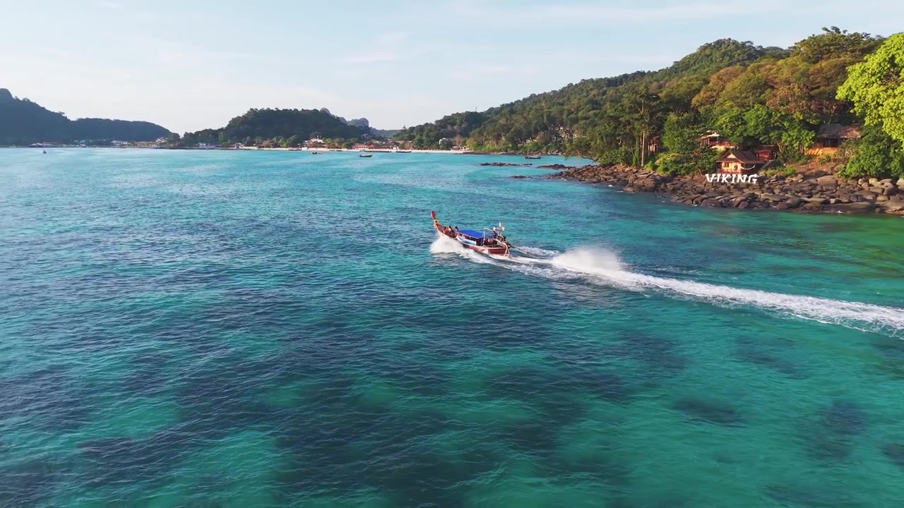 Aerea: barca longtail che naviga in una baia tropicale vicino alle Isole Phi Phi di giorno nello Stretto di Malacca, Thailandia, ripresa con drone in orbita