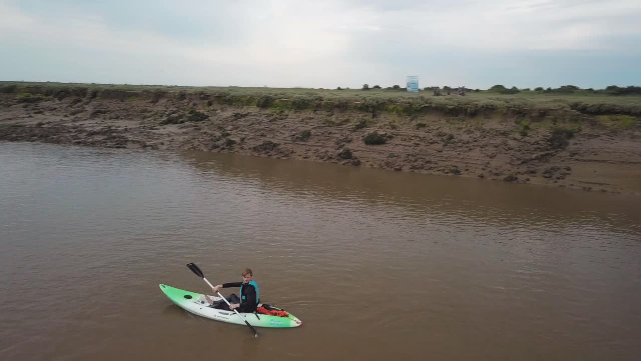 hombre navegando en kayak por un río serpenteante, drones rodean al kayakista