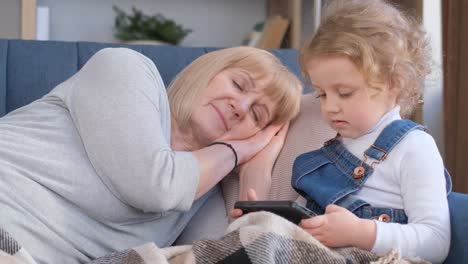 elderly woman and girl share smile while laying on couch holding hands a happy elderly woman is laying on a couch sharing a comforting arm around a little girl they smile sharing a tender gesture of love and leisure enjoying each others company