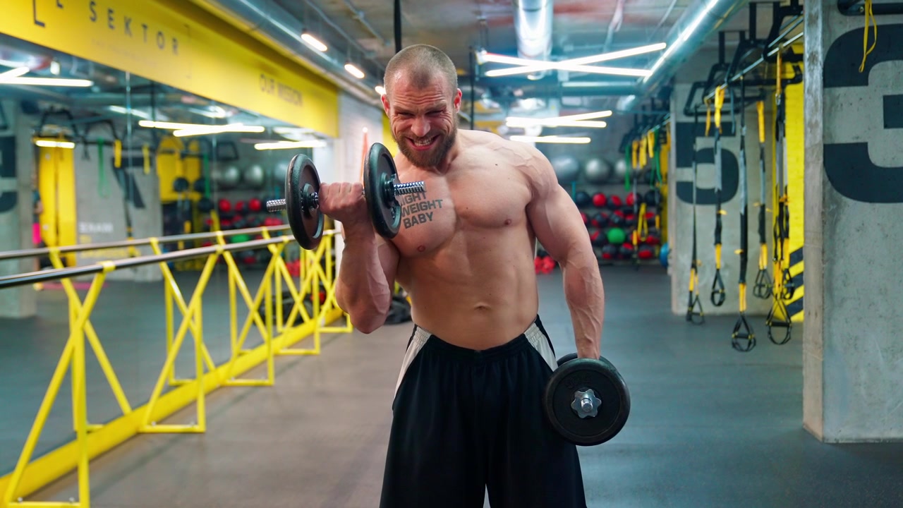 Uomo muscoloso che esegue curl bicipiti con manubri in palestra